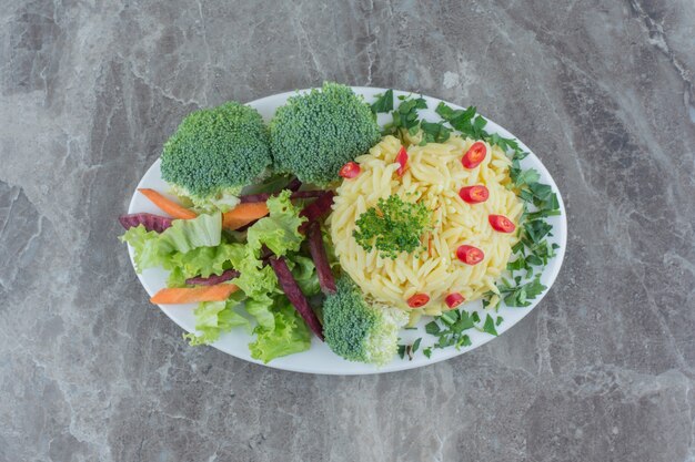 Pilau serving garnished by chopped pepper, cabbage, greens, carrot and broccolie pieces on a platter on marble.