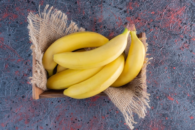 Pile of banana in wooden box on colorful surface