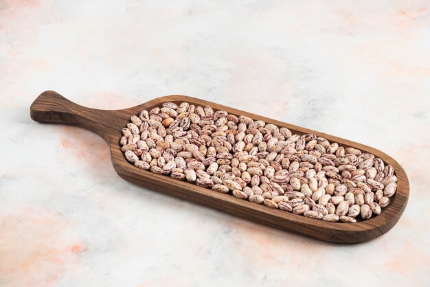 Pile of beans in wooden tray over white surface.