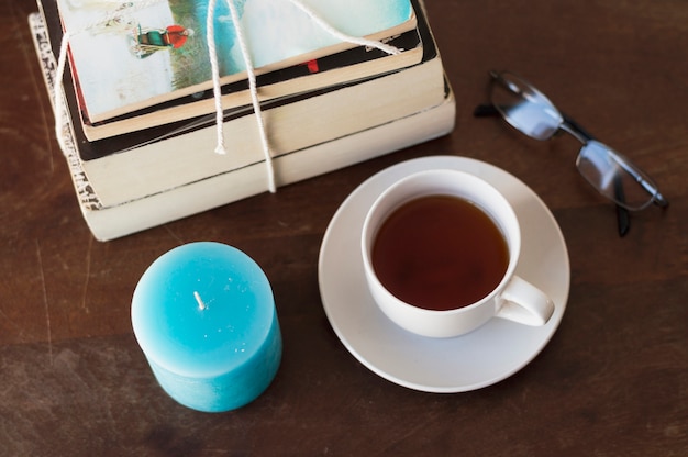 Pile of books, candle, coffee and glasses on table