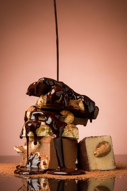 Pile of broken chocolate on table against brown studio background and hot chocolate spray