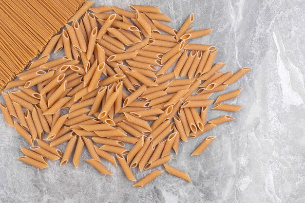 Pile of brown penne pasta placed on marble surface.