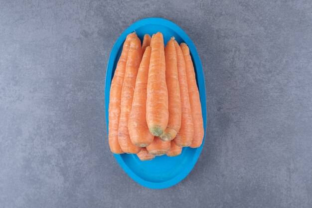 Куча моркови на синем подносе на мраморной поверхности.