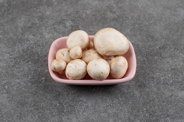 Pile of champignons in pink bowl over grey surface