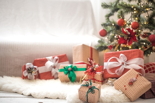 Pile of Christmas presents over light wall on wooden table with cozy rug. Christmas decorations