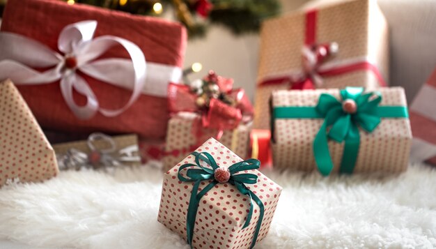 Pile of Christmas presents over light wall on wooden table with cozy rug. Christmas decorations