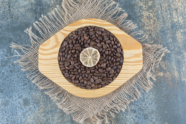 Free photo pile of coffee beans and lemon slice on wooden plate.