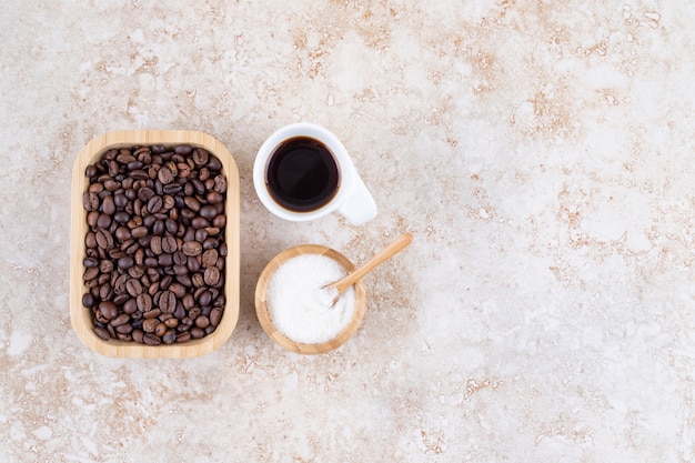 砂糖の小さなボウルとコーヒーのカップの横にある木製の大皿にコーヒー豆の山