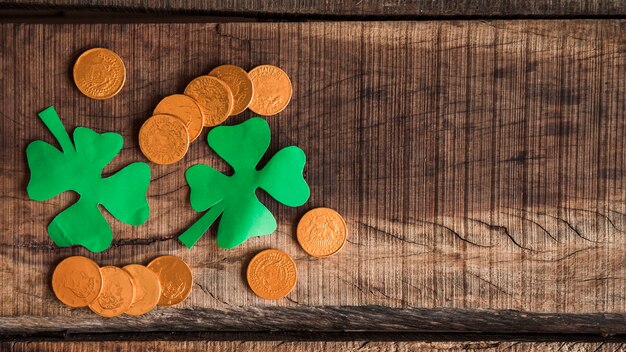 Pile of coins and paper shamrocks on wooden table