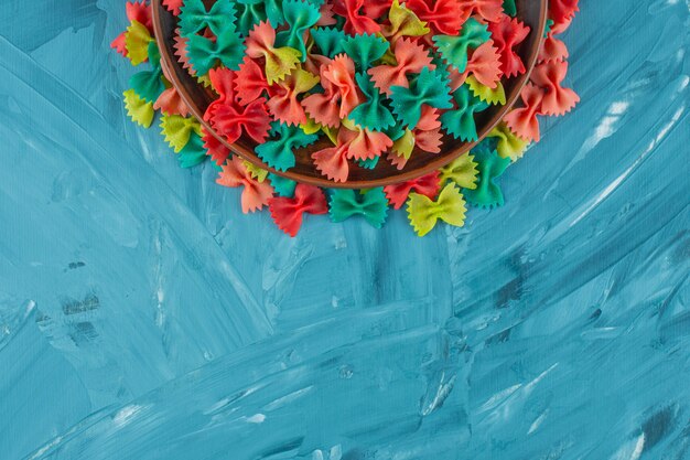 Pile of colorful raw farfalle pasta on blue background. 