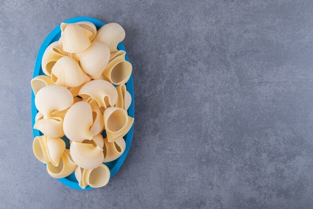 Foto gratuita mucchio di pasta conchiglie sul piatto blu.