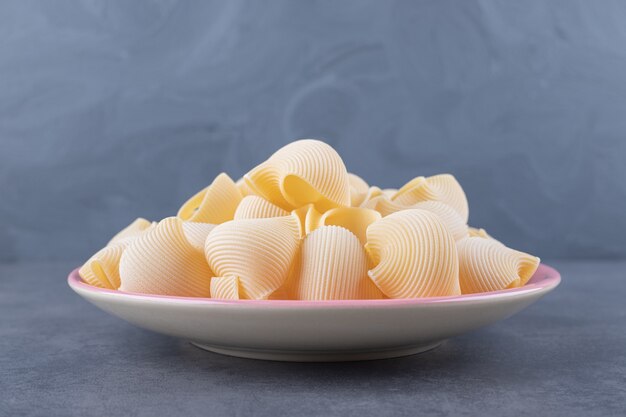 Pile of conchiglie pasta on pink plate. 