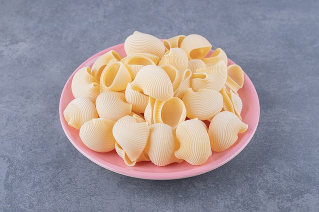 Pile of conchiglie pasta on pink plate.