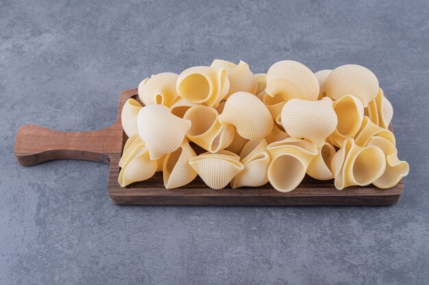 Pile of conchiglie pasta on wooden board.