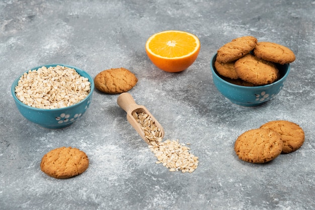 Pile of cookie and oatmeal in a bowl and half-cut orange over grey surface.