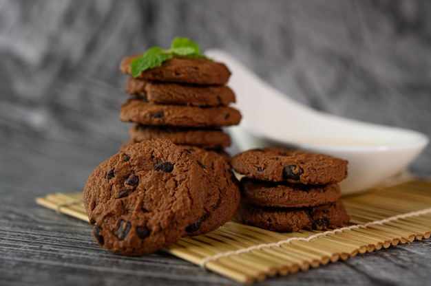 A pile of cookies and a spoon of milk on a cloth on a wooden table