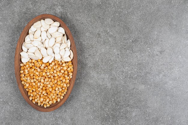 Pile of dried corns and pumpkin seeds on wooden plate.