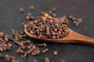 Free photo pile of dried natural cloves with wooden spoon on black surface.