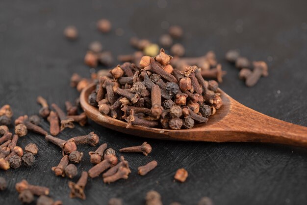 Pile of dried natural cloves with wooden spoon on black surface. 