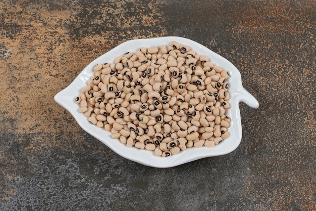 Pile of dry white beans on leaf shaped plate. 