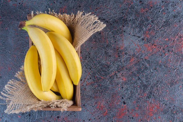 Куча свежих бананов в деревянной коробке на красочной поверхности