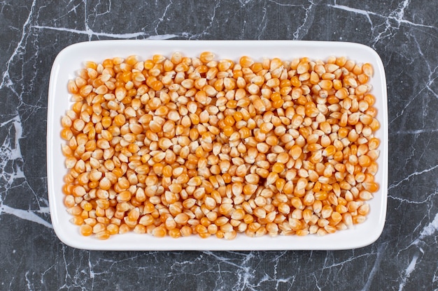 Pile of fresh corn seeds on white plate over black.