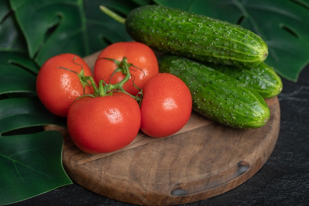 Pile of fresh organic vegetables. Cucumbers and tomatoes on wooden board with green leaves. 