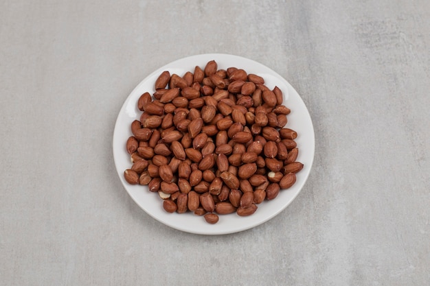 Pile of fresh peanuts on white plate.