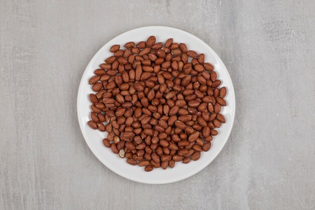 Pile of fresh peanuts on white plate.