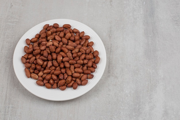 Pile of fresh peanuts on white plate.