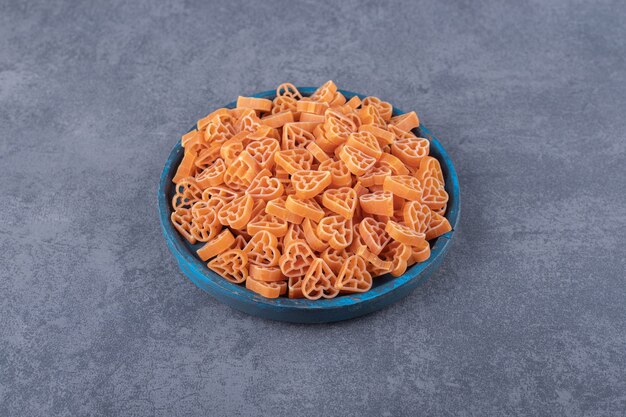 Pile of heart-shaped pasta on blue plate.