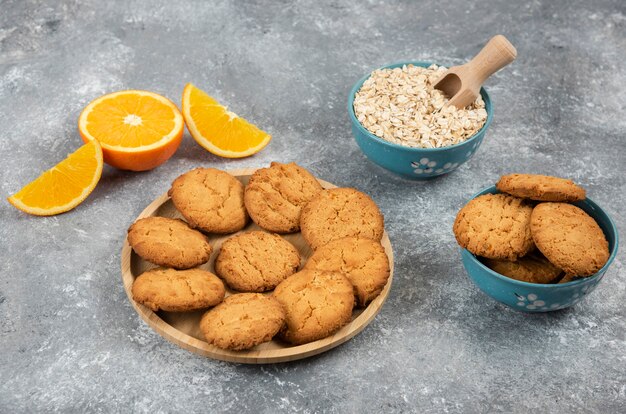 Pile of homemade cookies and oatmeal with orange over grey table.