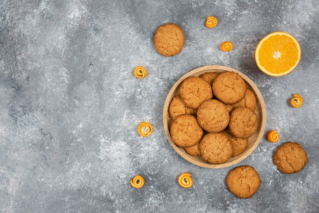 Pile of homemade cookies on wooden board and half cut orange.