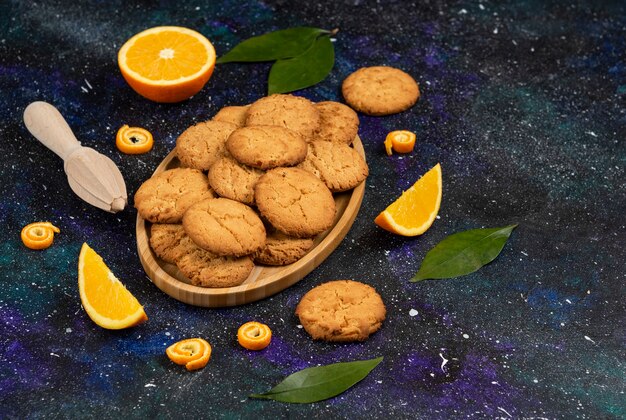 Pile of homemade fresh cookies and half cut or sliced orange over dark table.