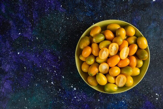 Pile of kumquats in ceramic bowl over blue surface