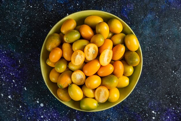 Pile of kumquats in ceramic bowl over blue surface