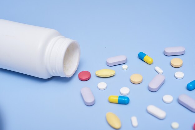 Pile of medical capsules pills in red and white color on blue surface, top view for copy space. White medical pills and tablets spilling out of a drug bottle. Macro top down view with copy space.