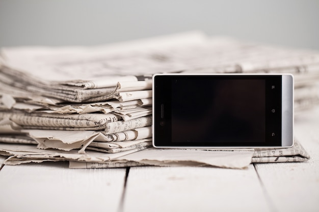 Free photo pile of newspapers with smartphone on it