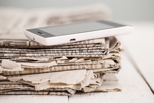 Free photo pile of newspapers with smartphone on it