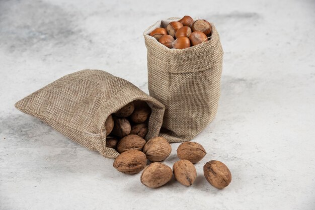 Pile of organic hazelnuts and walnuts in burlap on marble table. 