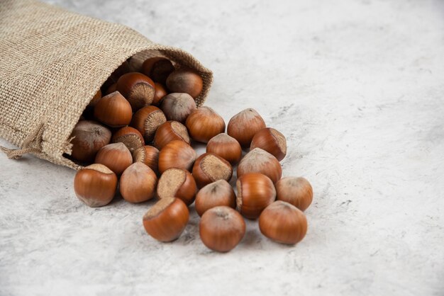 Pile of organic shelled hazelnuts in burlap on marble table. 