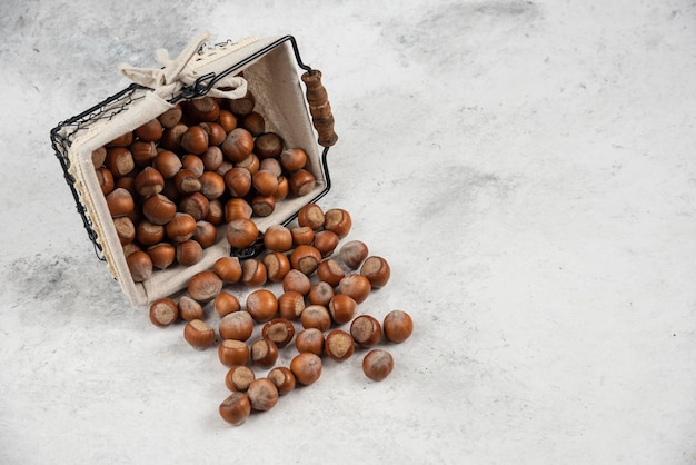 Free photo pile of organic shelled hazelnuts out of basket on marble table.