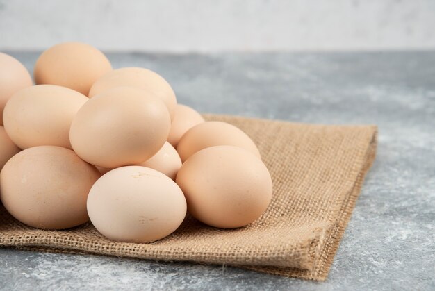 Pile of organic uncooked eggs with tablecloth on marble surface.