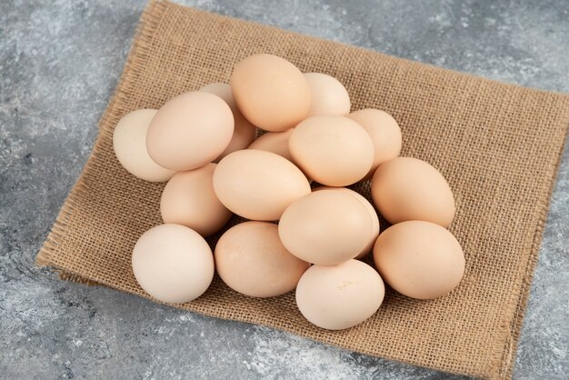 Pile of organic uncooked eggs with tablecloth on marble surface.