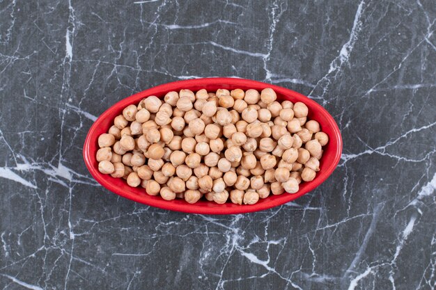 Pile of peeled hazelnuts in red bowl over black stone.