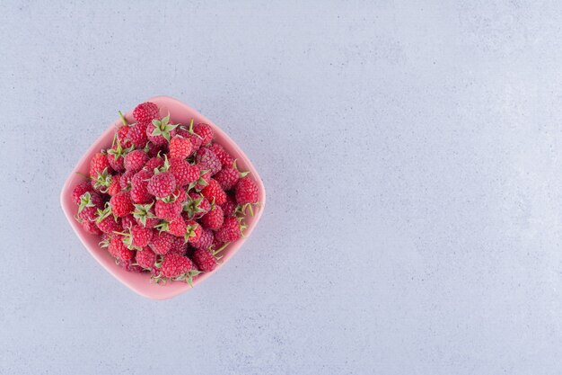 Pile of raspberries in a pink bowl on marble background.