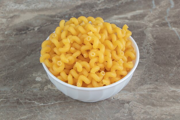 Pile of raw cellentani pasta in white bowl.