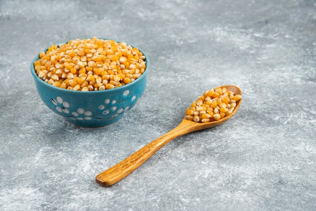Pile of raw corn seeds in blue bowls and wooden spoon.