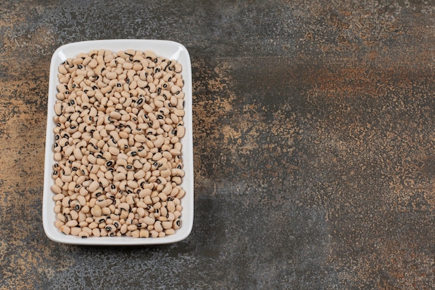 Pile of raw white beans on white plate. 