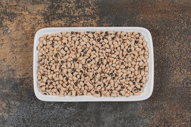 Pile of raw white beans on white plate. 